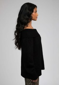 Pull noir en tricot surdimensionné avec un col côtelé large et des manches longues. Le mannequin l'associe à un pantalon imprimé léopard.