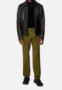 Giubbotto di pelle nera su un maglione nero, abbinato a pantaloni verde oliva e sneaker nere. Il look presenta un design elegante e su misura.