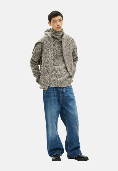 Maglione lavorato a maglia in marrone e crema con collo alto; abbinato a jeans in denim blu larghi; presenta una vestibilità oversize e un tessuto testurizzato.