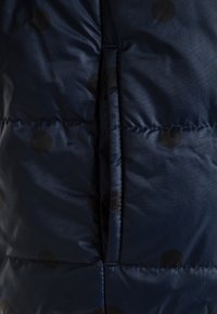 Gros plan sur un tissu matelassé bleu marine avec des pois noirs et une poche fendue verticale au centre.