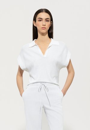 White knit top with a V-neck and short batwing sleeves, paired with light-colored, drawstring waist pants. Smooth texture, minimal design.