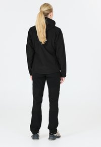 Musta ulkoilutakki ja housut slim fit -mallissa. Takissa on korkea kaulus, ja housuissa on vahvistetut paikat. Molemmat ovat valmistettu kestävästä kankaasta.