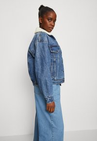 Spijkerjack met een schapenvachtkraag, met een relaxte pasvorm, lichtblauwe kleur, zijzakken en knoopsluitingen, gecombineerd met bijpassende jeans.