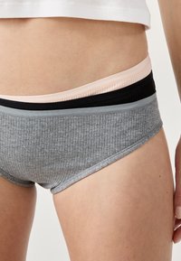 Des bandes de sous-vêtements en coton à rayures empilées, de couleur gris, noir et rose clair, sur la taille et la cuisse supérieure d'une personne.