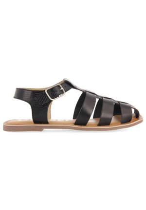 Black flat sandal with three front straps, ankle buckle strap, and tan sole, shown from the side on a white background.