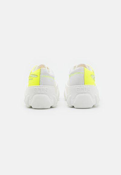 Λευκά αθλητικά παπούτσια με παχιά σόλα, που διαθέτουν φωτεινή κίτρινη λεπτομέρεια και υφασμάτινες αερόπετρες στην φτέρνα για αναπνοή. Με ανάγλυφο λογότυπο.