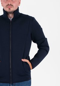 Giacca navy con zip e collo alto, realizzata in tessuto testurizzato. Presenta tasche laterali e un design aderente.