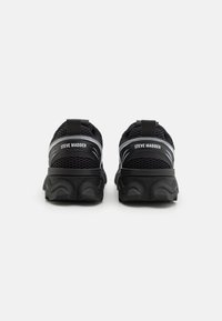 Sneaker in mesh nero con una suola spessa e testurizzata. Presenta un bordo di trazione e un marchio bianco sul tallone. Design elegante con accenti sottili.