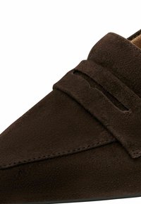 Mocassin en daim brun foncé avec une bride à pièce et des coutures visibles le long de l'embout arrondi et du quartier.