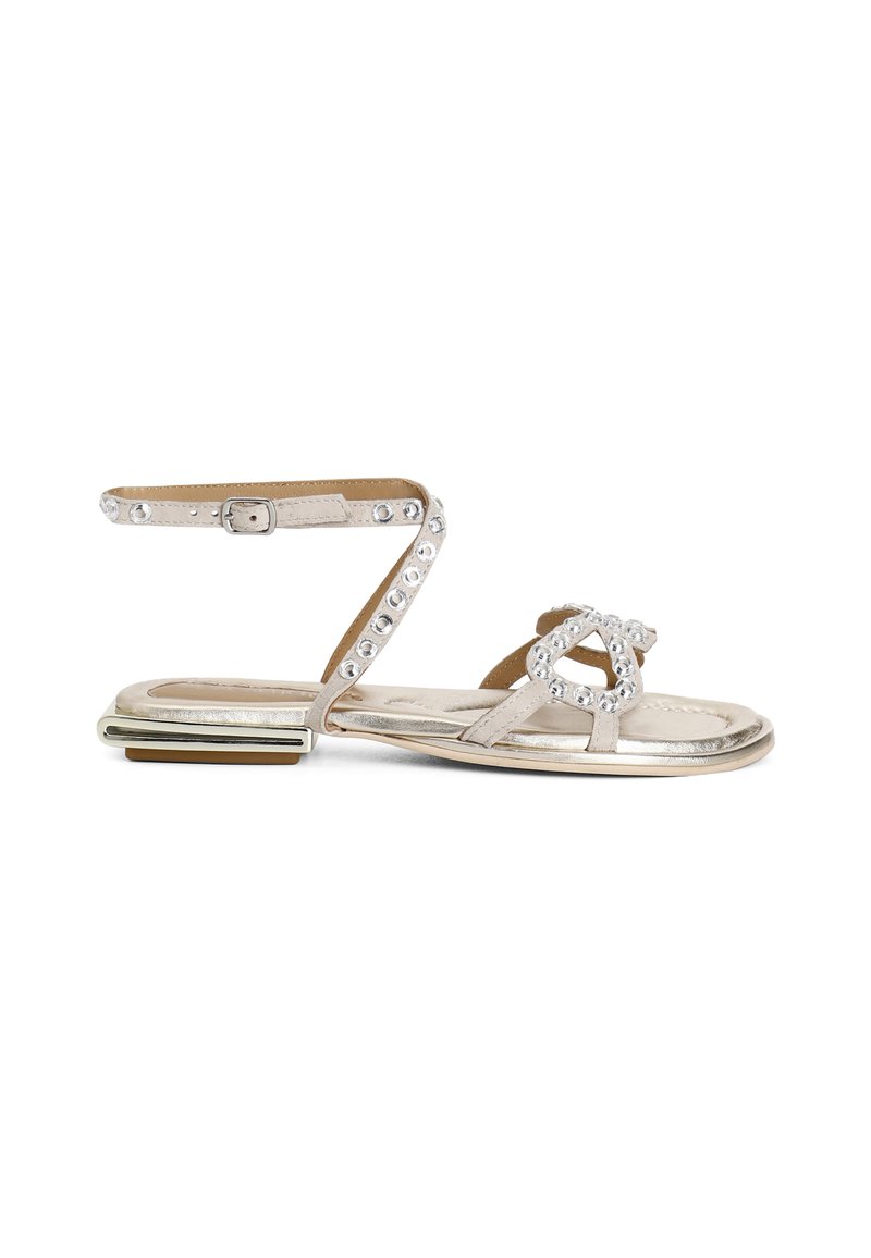 Sandalo piatto con cinturini in argento metallico, dotato di un design a doppia fascia, impreziosito da pietre preziose trasparenti e una suola con accenti dorati.