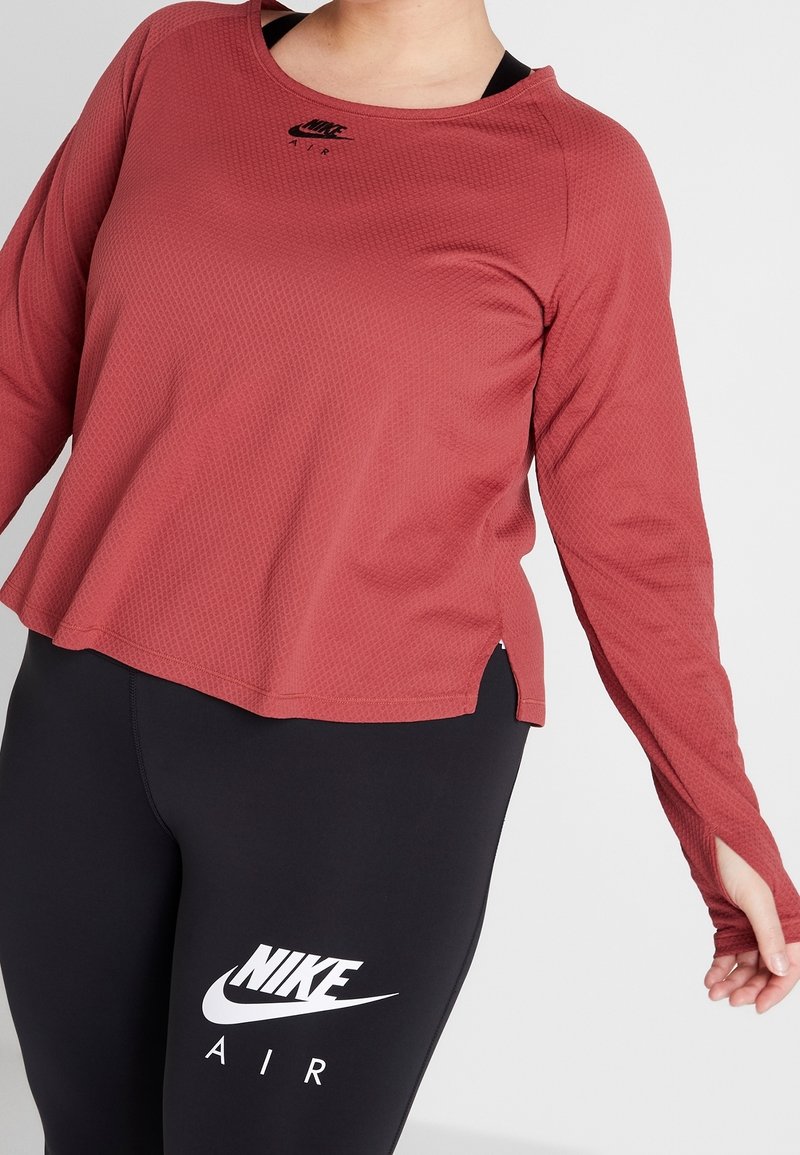 Rode, gestructureerde lange mouwen sporttop met een ronde halslijn, zijslitsen en zwart Nike-logo. Draagt een zwarte legging met witte Nike-branding.