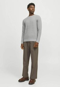 Suéter de punto gris claro con un patrón texturizado, combinado con pantalones marrones de corte holgado y zapatos marrones oscuros.