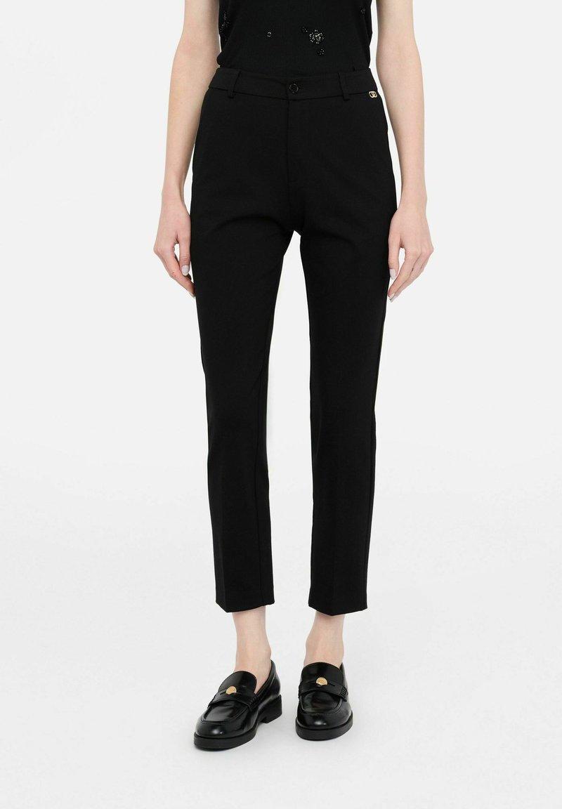 Pantaloni neri sartoriali a taglio slim, con chiusura a bottone, passanti per cintura e un sottile dettaglio logo dorato. Tessuto dalla texture liscia.