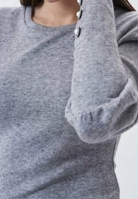 Maglione grigio lavorato a maglia con scollatura rotonda e maniche a sbuffo. Presenta quattro bottoni decorativi in perla lungo la manica. Tessuto morbido.