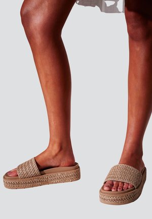 Legs wearing beige woven platform slide sandals with thick soles and open toes against a plain background.
