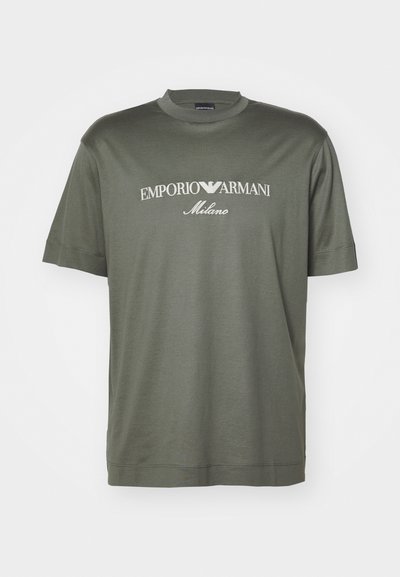 T-shirt de algodão verde-escuro com gola redonda, apresentando um logo branco com a inscrição "EMPORIO ARMANI Milano" na parte da frente. Mangas curtas.
