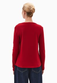 Czerwona bluzka z długim rękawem, wykonana z miękkiego materiału, z okrągłym dekoltem i luźnym krojem, zestawiona z ciemnymi dżinsami.