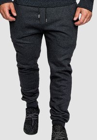 Dunkelgraue Jogginghosen aus weichem Stoff, mit elastischen Bündchen, einem Kordelzugbund und seitlichen Taschen. Getragen mit strukturiertem schwarzen Schuhwerk.