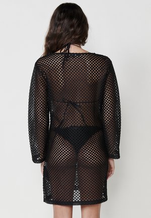 Black mesh cover-up with long sleeves, featuring a fishnet pattern and an open back design, highlighting an underlying swimsuit.