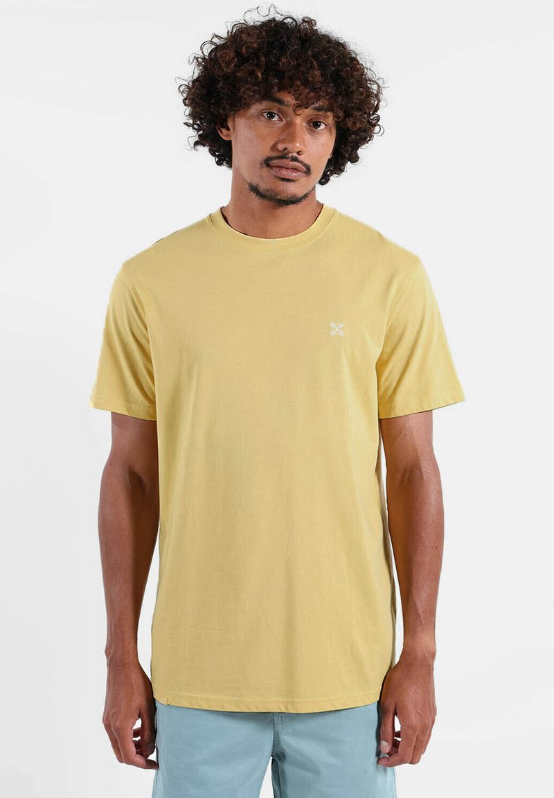 T-shirt en coton jaune avec un col rond, manches courtes, comportant un petit logo blanc sur la poitrine gauche. Texture lisse.