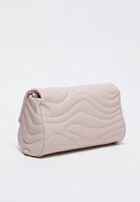 Beige, gewatteerde handtas met een zachte textuur, gekenmerkt door golvende oppervlaktepatronen en een strak ontwerp, gesloten met een goudkleurige rits.