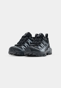 Paire de chaussures de trail running noires et grises avec semelles robustes et système de laçage rapide sur fond blanc uni.
