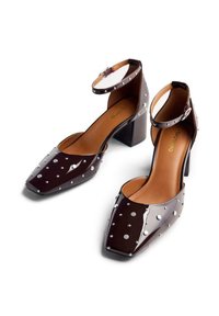 Zapatos de tacón alto de charol marrón, con puntera cuadrada, correa en el tobillo y acentos de tachuelas plateadas en la superficie exterior. Diseño de tacón en bloque.