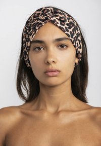 Fascia della testa in tessuto animalier, caratterizzata da un design frontale attorcigliato, con una texture liscia e una palette di colori neutri in beige e nero.