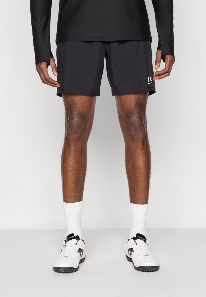 Μαύρο αθλητικό σορτς από αεριζόμενο ύφασμα, εφαρμοστό σχέδιο, μήκος πάνω από το γόνατο, συνδυασμένο με λευκές κάλτσες και μαύρα αθλητικά παπούτσια. Ορατό το λογότυπο της Under Armour.
