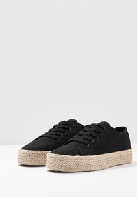 Baskets en toile noire avec une surface texturée et une semelle plateforme en jute tissé. Elles présentent des lacets ronds et des œillets en métal pour la fermeture.