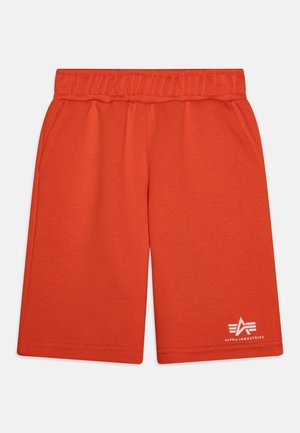 Calções vermelhos até à cintura feitos de tecido suave, apresentando uma faixa elástica na cintura e bolsos laterais. Logotipo notável impresso perto da bainha.