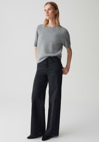 Maglione grigio in maglia soffice con maniche corte abbinato a jeans neri a vita alta e gamba larga, insieme a scarpe nere a punta. Design semplice e moderno.