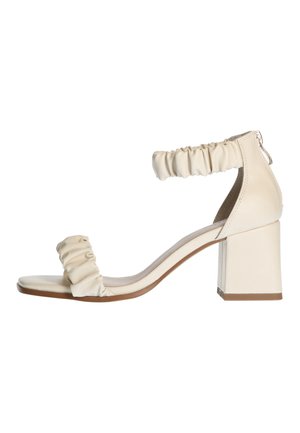 Beżowa sandałka na słupku, z falbankowym paskiem wokół kostki i gładkim paskiem na palcach, cechująca się minimalistycznym designem.