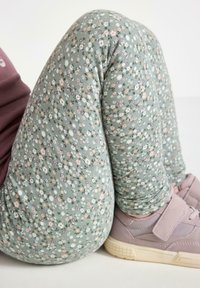 Gröna leggings med ett litet blommönster i vitt, rosa och gult, kombinerat med ljuslila sneakers med ett kardborreband.