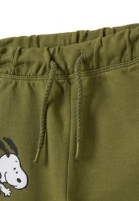 Pantaloni sportivi verde oliva con vita elastica, dotati di cordino e una grafica nera di Snoopy sul lato sinistro. Texture liscia.