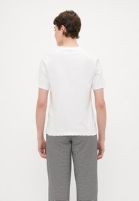 White cotton t-shirt with short sleeves, standard fit, straight hem, worn with black and white striped pants, minimalistic design.