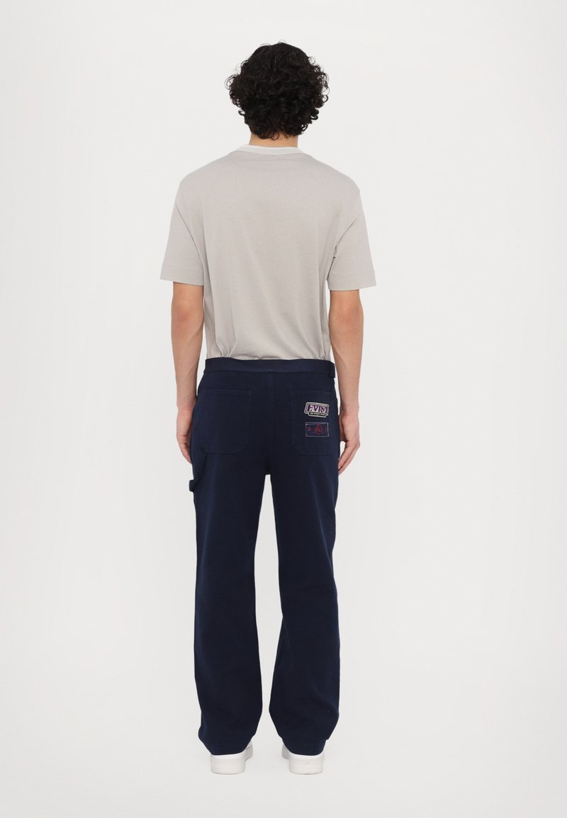 Pantalones azul marino con un diseño de pierna recta, que presentan bolsillos y una etiqueta en el parche trasero. Combinados con una camiseta de manga corta en gris claro.