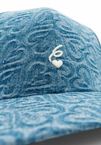 Jeanskepp med ett texturerat blått tyg, med en vit broderad logotyp och hjärtdetalj på framsidan. Böjd skärm, strukturerad form.