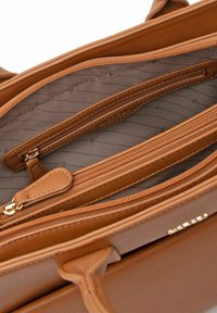 Interno di una borsa a mano in pelle marrone con più scomparti, dotata di chiusure con cerniera e rivestimento in tessuto con motivi sottili.