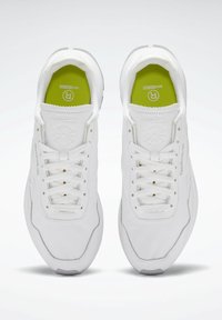 Vita sportskor med en slät läderöverdel, texturerade detaljer, snörning framtill och gröna innersulor med en logotyp.