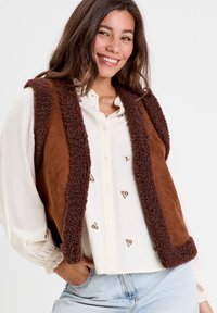 Gilet marrone senza maniche con un rivestimento interno morbido e una superficie esterna liscia. Presenta un design accogliente e bordi di tono marrone a contrasto.