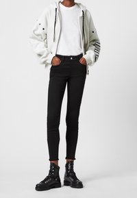 Vit zip-up hoodie med svarta detaljer, kombinerad med svarta slim-fit jeans och svarta snörade kängor. Outfiten betonar en avslappnad stil.