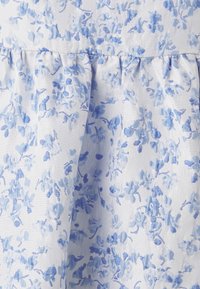 Tissu floral bleu clair avec un motif texturé ; présente de petites fleurs sur fond blanc, avec des détails froncés à l'ourlet.