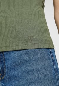 Canotta a costine verde oliva con un discreto logo ricamato 'Lee' sull'orlo, abbinata a jeans in denim blu classici.