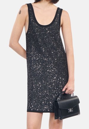 Zwarte mouwloze jurk met een losse pasvorm, versierd met verspreide zilveren pailletten; gecombineerd met een gestructureerde zwarte handtas.