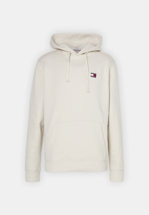 Kremowa bluza z kapturem z przednią kieszenią, regulowanymi troczkami i małym czerwono-biało-czarnym logo Tommy Jeans na lewym piersi.