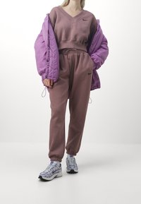 Lila puffjacka, brun sweatshirt med V-ringning, matchande joggers och sneakers med lila detaljer; mjukt tyg med elastiska manschetter.