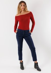 Body off-shoulder rosso a maniche lunghe abbinato a pantaloni slim-fit blu navy e stivali neri alla caviglia con cerniere. Design semplice e aderente.