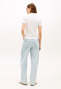Polo blanc à manches courtes avec une silhouette ajustée, associé à un jean large taille haute bleu clair et des sandales plates. Design minimaliste.