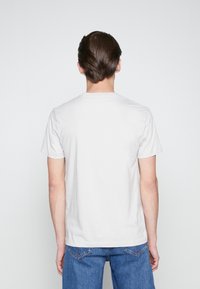 Ljust grå t-shirt med kort ärm och rund hals, visad bakifrån. Slät textur, avslappnad passform, tillsammans med blå denimjeans.